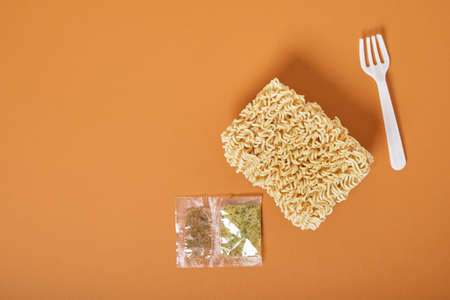 white disposable plastic fork, three block of dry instant noodles and spices on a brown background top view copy spaceの写真素材