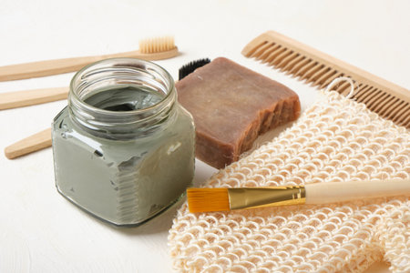 soap, blue clay in a glass jar, brush, washcloth and bamboo toothbrushes on a beige background, copy...