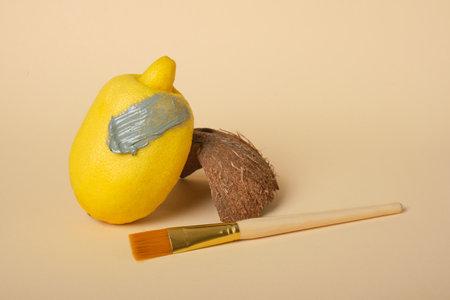 lemon smeared with cosmetic clay, coconut shell and a brush for applying clay, beige background,...