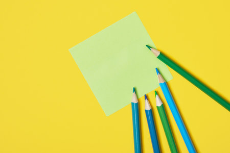 several colored pencils and sticky notes on yellow background copy space top viewの写真素材
