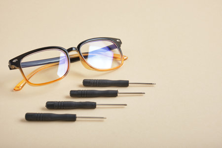 eye glasses and small screwdrivers on a beige backgroundの写真素材