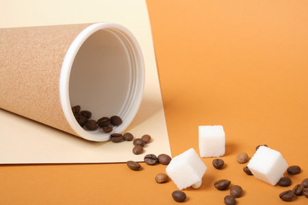 Thermo mug, scattered coffee grains and white sugar cubes on brown and beige geometric background copy spaceの写真素材