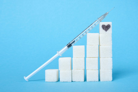 insulin syringe and a ladder of white sugar cubes on a blue background, a heart is drawn on the sugarの写真素材