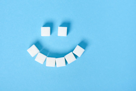 White sugar cubes laid out in the form of a sad smile on a blue background close-up, copy space. diabetes conceptの写真素材