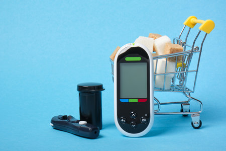 glucose meter and brown and white sugar cubes in a shopping cart on a blue background copy spaceの写真素材