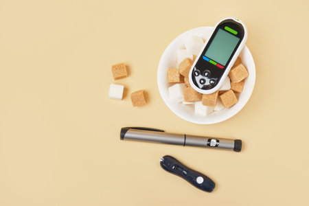 blood glucose meter, lancet, insulin syringe pen and sugar cubes in a white bowl on a beige...