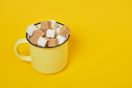 cane brown and white sugar cubes in yellow cup on yellow background copy spaceの写真素材