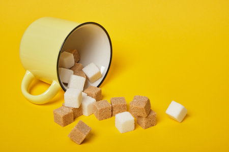 cane brown and white sugar cubes dropped out of yellow cup on yellow background copy spaceの写真素材