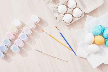 process of painting eggs for easter, eggs box, easter eggs, plate, brushes and paints on the table top viewの写真素材