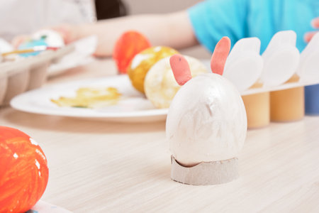 process of painting eggs for easter, eggs box, easter eggs, plate, brushes and paints on wooden tableの写真素材