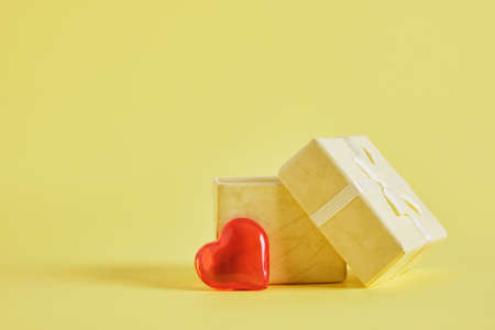 small red smiling heart and open yellow gift box on yellow background copy spaceの写真素材