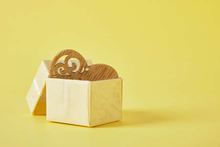 wooden heart in small open yellow gift box on yellow background copy space