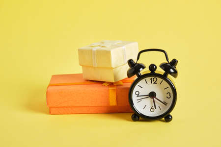 Black retro alarm clock and gift box yellow background copy space. concept of congratulation time