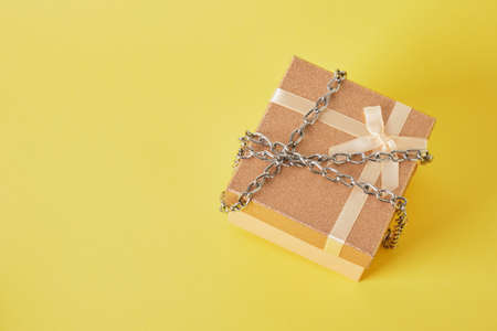 shiny pink square gift box wrapped with chain on yellow background protection of the gift. prohibition to openの写真素材