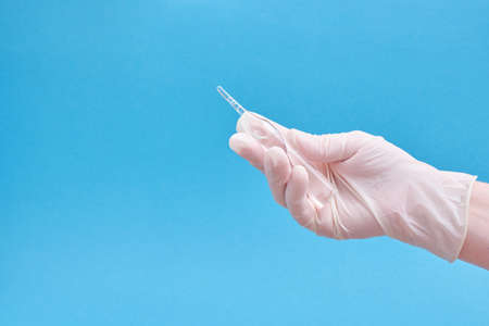 Ampoule with a medicine or vaccine and a syringe in hands in rubber gloves on a blue background blue...