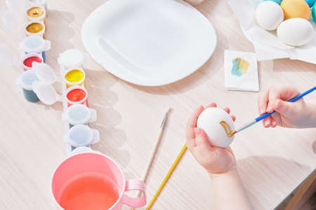 child paints egg for Easter on a wooden table,の写真素材