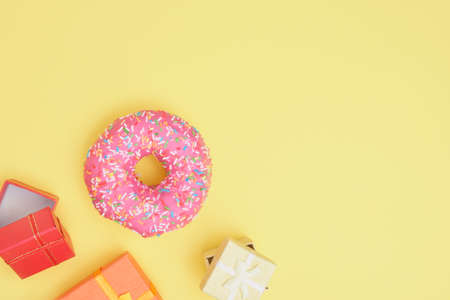 donut with sprinkles and pink icing and several different gift boxes on a yellow background top view...