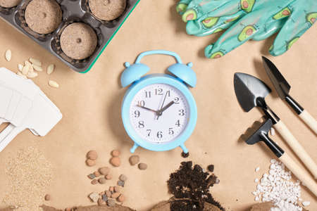 alarm clock and gardening tools on kraft paper place copy top view time for spring planting...