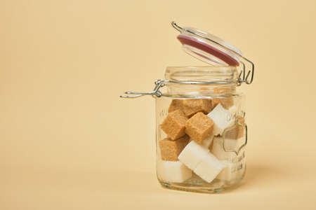 brown and white sugar cubes in a jar with a sealed lid, beige background copy spaceの写真素材