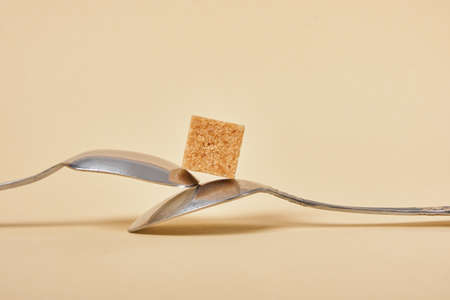 metal spoon with brown sugar cube on beige background, health care and diabetes concept copy space