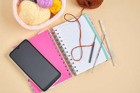 smartphone, notebook and knitting hooks and threads in a basket on a beige background, online...