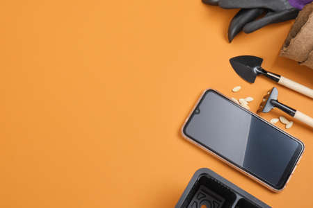 smartphone and garden equipment on brown background, gardener blog concept, seeds, pots, shovels and garden gloves, place copy top viewの写真素材
