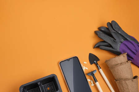 smartphone and garden equipment on brown background, gardener blog concept, seeds, pots, shovels and garden gloves, place copy top viewの写真素材