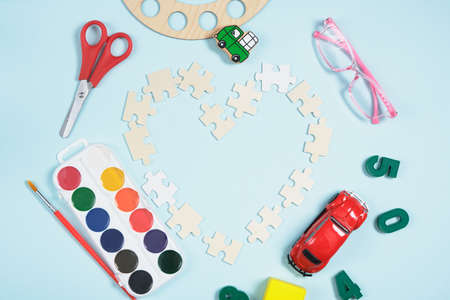 heart made of wooden puzzles and various school accessories on a blue background, paints, childrens...