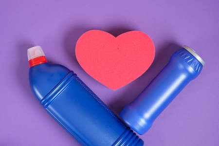 red heart shape sponge and detergent bottles without labels on purple background copy sapce top view cleaning set conceptの写真素材