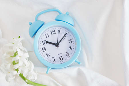 blue alarm clock and flower on bed, spring morning mood concept copy space