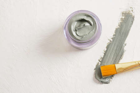 a brush for applying face masks, a jar of cosmetic blue clay and a smear of clay on a textured light background copy space top viewの写真素材