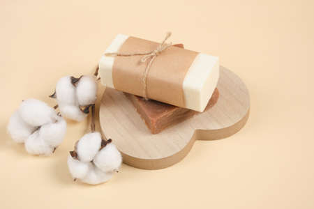 two bars of homemade handmade soap on a wooden stand in the shape of a heart and a cotton flower beige backgroundの写真素材