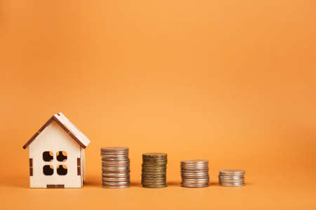 small wooden house model and several towers of coins on a brown background sale and purchase of real estate concept, construction or rent of houseの写真素材