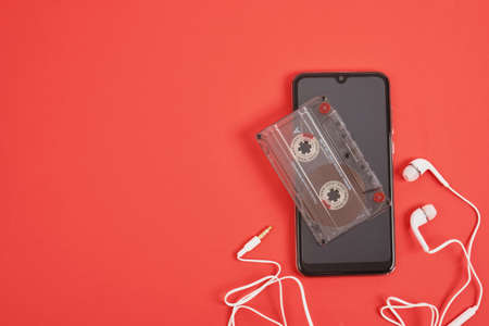 smartphone headphones and audio cassette on red background, memories concept, modern technologies...