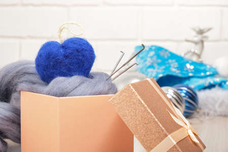 blue felted woolen heart of a needle and a skein of wool in a gift box on the table, felting Christmas tree decorations, heart on the treeの写真素材
