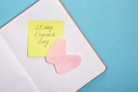 notepad, silhouette of the thyroid gland cut out of pink felt and yellow sticker on a blue background, nutrition for diseases of the thyroid gland concept copy spaceの写真素材