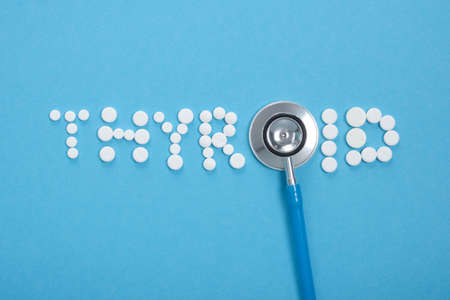 inscription of thyroid gland from white pills and stethoscope on blue background, diagnosis and...