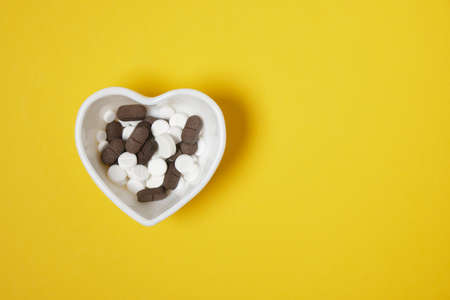 white and brown pills in a small heart-shaped plate yellow background copy spaceの写真素材
