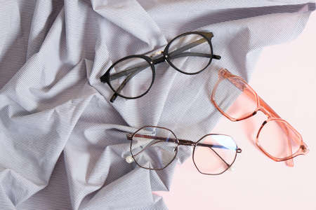 several stylish eye glasses on a striped fabric on a pink background copy space, eye glasses on a...