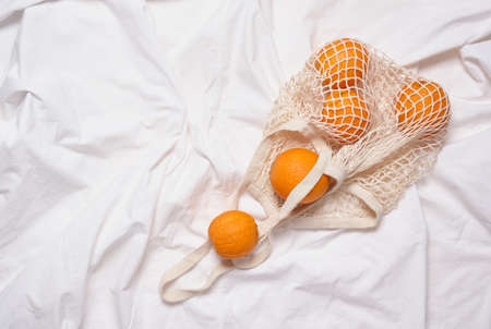 mesh eco bag with oranges on white cloth backgroundの写真素材