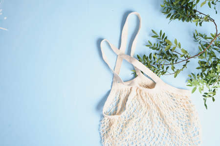 Reusable mesh shopping bags and green leaves on blue background. Zero waste concept.の写真素材