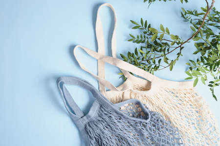 Reusable mesh shopping bags and green leaves on blue background. Zero waste concept.の写真素材