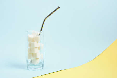 metal reusable cocktail tube and cubes of white sugar in a glass, light blue and yellow background copy space, high sugar content in drinks and food conceptの写真素材