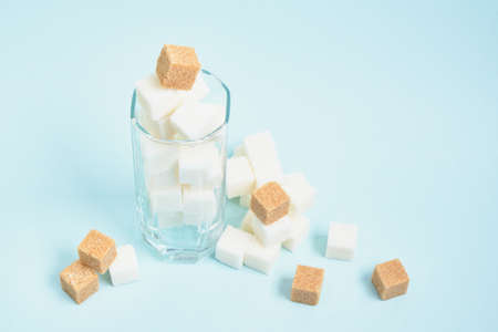 cubes of white and brown sugar in a glass and on a light blue and beige background copy space, sugar in drinks and food conceptの写真素材