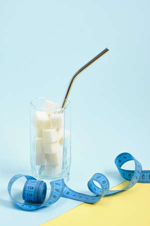 measuring tape and glass with sugar cubes and cocktail tube light blue and yellow background copy space, overweight and malnutrition conceptの写真素材