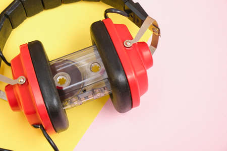 old red headphones and tape cassette on pink background copy space
