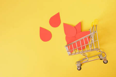 paper drops of blood and shopping trolley on yellow background, world donor day concept, donate...