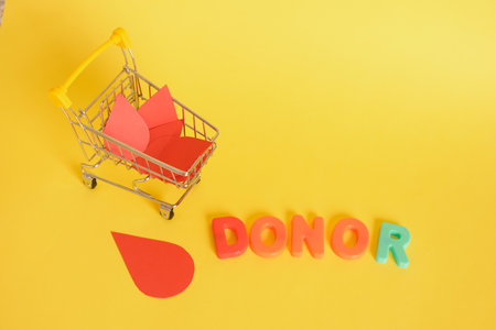 paper drops of blood and shopping cart and inscription donor on yellow background, world donor day...