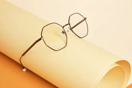 trendy eye glasses on rolled beige paper, geometric background, trending colors, yellow background...