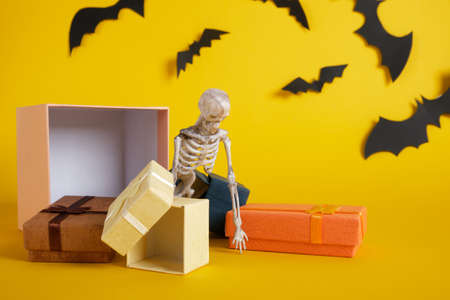 plastic skeleton and gift boxes on yellow background, halloween concept, skeleton fell out of gift box, skeleton crawling over giftsの写真素材